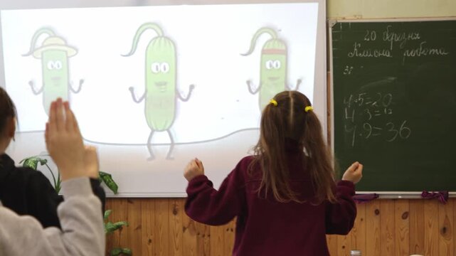 Primary school children dancing to an interactive animated video in a classroom, where students engage with a projector screen to foster a dynamic and collaborative learning environment