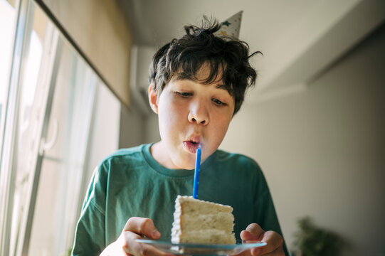 A teenage boy blows out a candle on a cake indoors