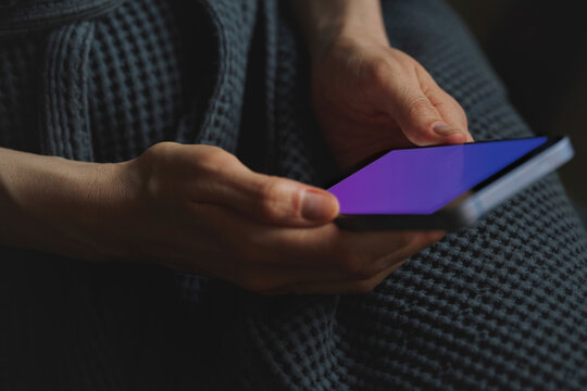 A woman in a waffle robe holds a smartphone with a neon screen