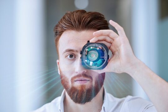 Young businessman looking through open camera lens at office