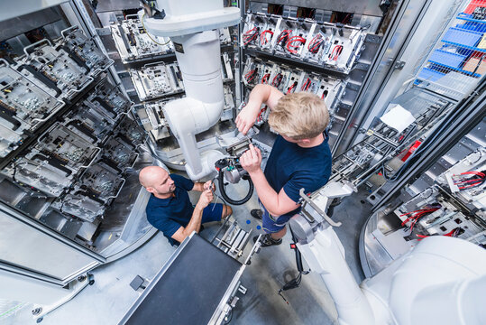 Two colleagues working at industrial robot in modern factory