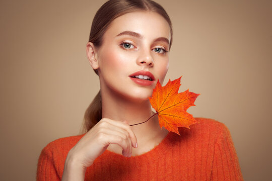 Portrait of beautiful young woman in orange blouse with autumn leafs. Healthy clean fresh skin natural make up beauty eyes