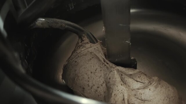 Woman baker uses scraper to separate and remove piece of cooked dough from bowl of industrial mixer. Process of baking bread in commercial kitchen. Dough preparation activity, food industry