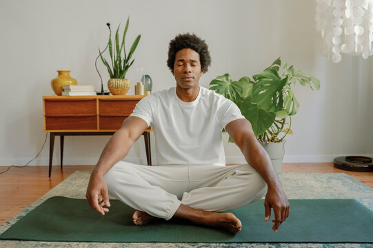 Man with eyes closed doing yoga on exercise mat at home in morning