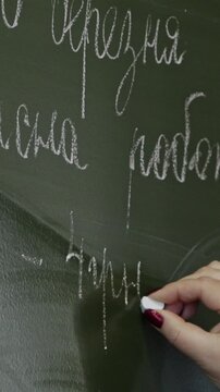 A hand writes cursive script using white chalk on a green classroom blackboard, representing academic instruction, learning, pedagogical effort, and traditional education. Vertical
