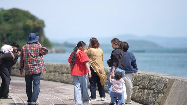 Group of friends stroll seaside promenade. They laugh, share smiles, and enjoy the view. Sky is clear, sea waves gently lap the shore. Perfect for travel, family, or friendship themes