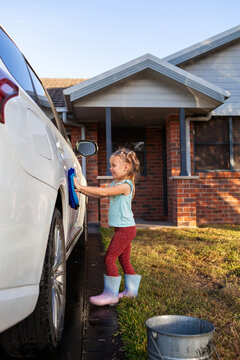 Young child helping wash family car parked on driveway in suburban front yard