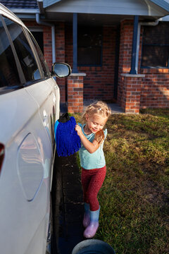Young child helping wash family car parked on driveway in suburban front yard