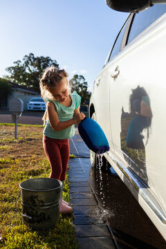 Young child helping wash family car parked on driveway in suburban front yard