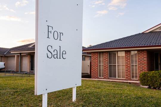 for sale sign outside house in suburb at dusk
