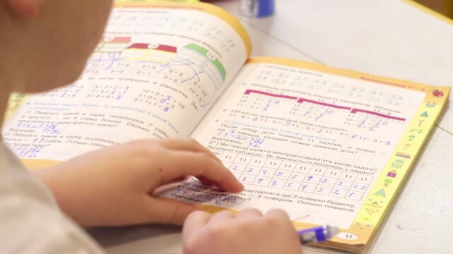 A schoolchild solving math exercises in a textbook at a classroom desk, highlighting academic focus, early childhood education, learning process, and daily student development activity