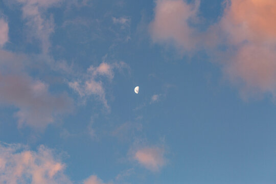 Half moon in sky framed by sunset clouds