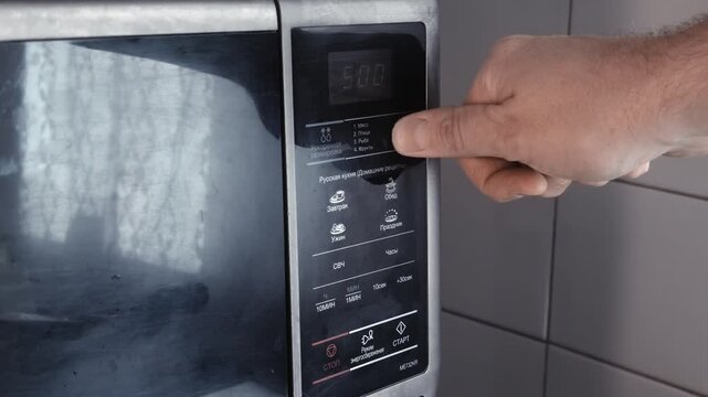 Male hand operating touch control panel of microwave oven. Setting cooking time and power using finger pressing digital interface buttons