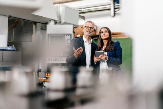 Businessman an woman in high tech enterprise, having a meeting in factory workshop