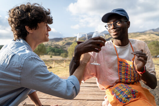 Two friends clink glasses outdoors, smiling warmly. Two friends clink glasses outdoors, smiling warmly