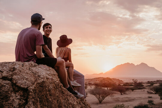 Namibia, Spitzkoppe, friends sitting on a rock at sunset