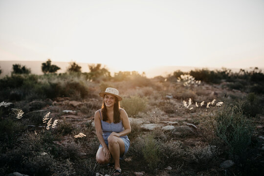 Smiling woman crouching in field at sunset
