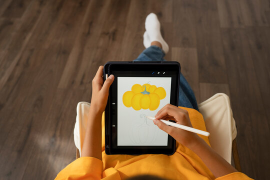 Girl drawing yellow pumpkin on tablet PC with digitized pen at home