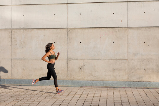 Young woman running along concrete wall in the city