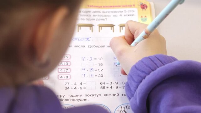 A small child in purple clothes solves elementary school math problems in a workbook using a pencil, illustrating academic focus, early childhood education, and diligent home study