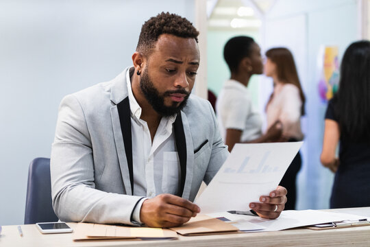 Young entrepreneur analyzing document with colleagues in background at office