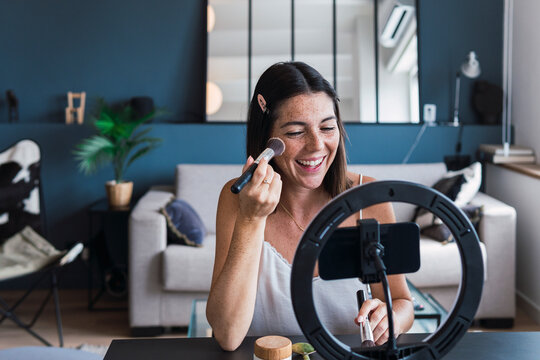 Happy influencer recording make-up tutorial on smart phone at home