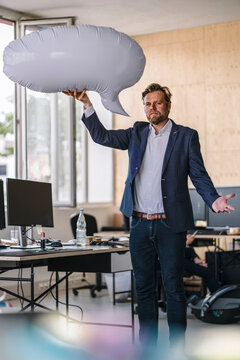 Businessman standing in office, holding inflatable speech bubble