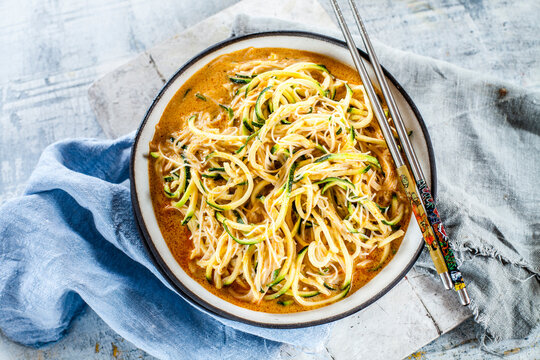 Asian style noodle soup with glas noodles and zoodles in red curry broth