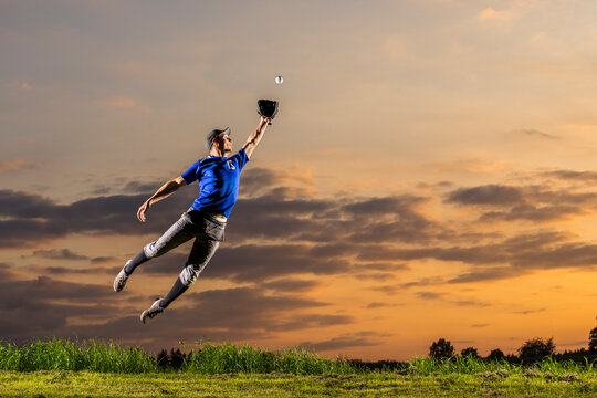 Young man jumping and catching baseball at dusk