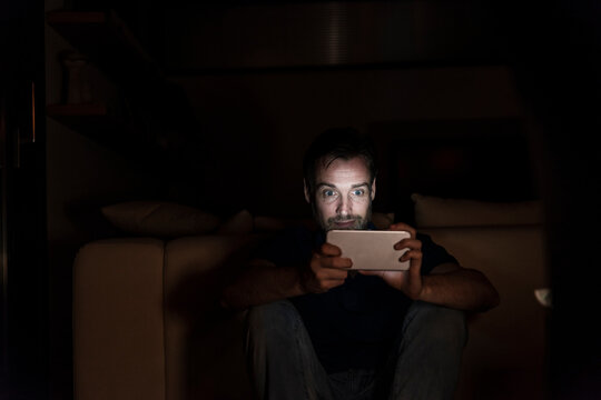 Man sitting in the dark at home starring at smartphone