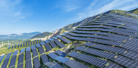 Naklejka premium Large-Scale Solar Photovoltaic Farm Installed on Mountain Slopes Under Clear Blue Sky