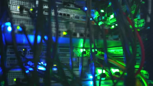 Close-up reveal of dark data center server racks filled with dense cable bundles and glowing blue and green LED indicator lights on active network hardware