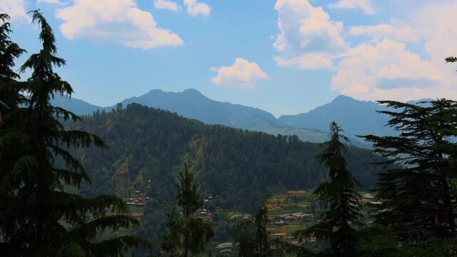 4K shot of clouds above the Himalayan mountain range with Pine trees as seen during the summer season from Peej village in Kullu district, Himachal Pradesh, India. Summer in Himalayas background.