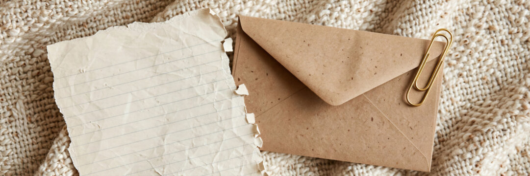 Realistic paper collage flat lay featuring ripped notebook sheet and brown envelope on cozy woven wool blanket