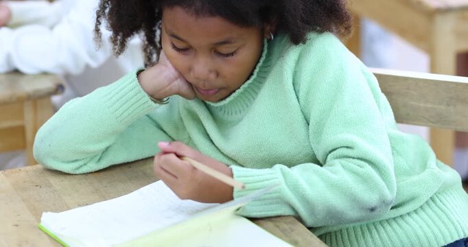 Focused schoolgirl writing in a classroom during a learning activity. Back to school concept featuring education, concentration, creativity, childhood, and academic development, close-up