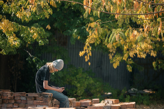 A young individual wearing a beanie and casual clothing is engrossed in their smartphone