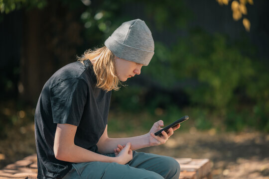 Teenager wearing a beanie and black t-shirt looking at their phone outdoors