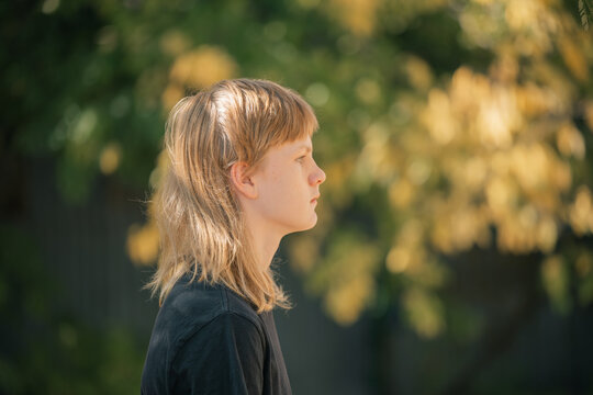 Young person with a mullet hairstyle looking thoughtfully into the distance outdoors