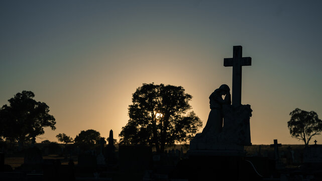 Silhouette of a weeping angel statue at a cemetery during a serene sunrise