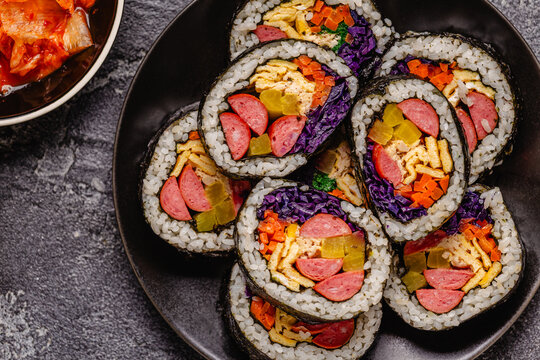 A black plate filled with kimbap (or gimbap) that have colorful fillings.