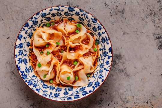 Wontons are placed in a bowl with spicy sauce.