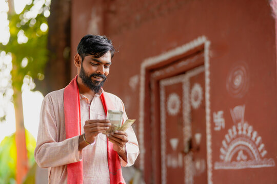young indian farmer counting money standing on village wall background