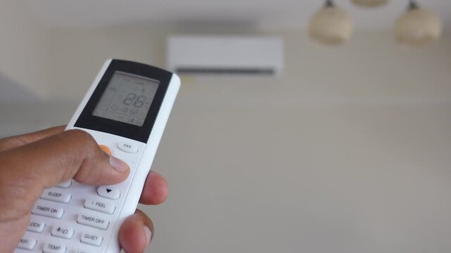 Person using air conditioner remote control to adjust temperature indoors