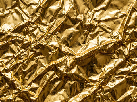 Abstract texture of shiny crumpled rose gold foil paper with deep shadows and bright highlights