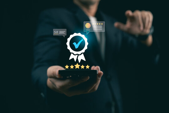 Businessman holding smartphone with glowing quality assurance badge and customer satisfaction rating icons, concept of premium mobile service.