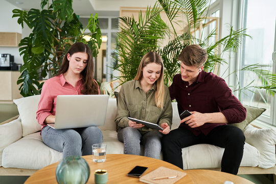 Smiling female intern discussing over digital tablet with businessman while sitting by female colleague in office