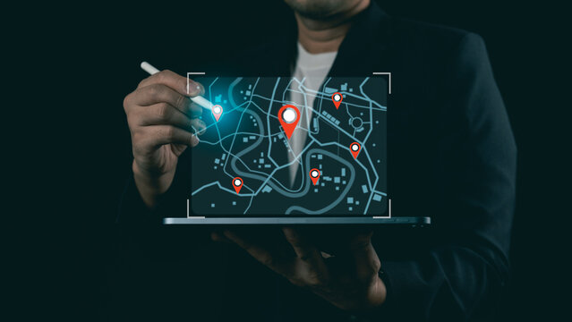 Businessman using stylus pen with glowing digital city map and pin pointers on laptop screen, concept of navigation and logistics tracking.