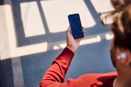 Hand holding smartphone with declining stock market chart outdoors