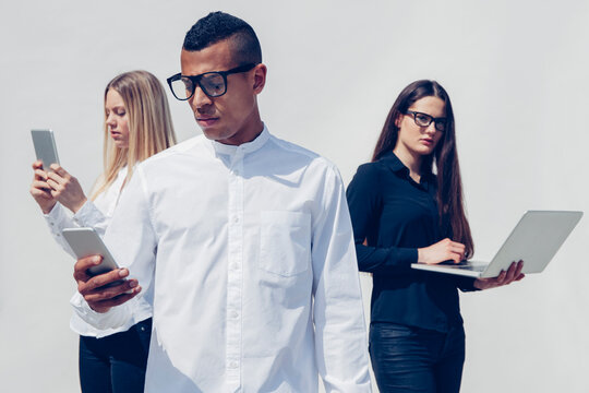 Three stylish young people with mini tablet, smartphone and laptop in front of white background