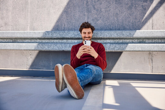 Smiling while sitting outdoors using a smartphone in the city
